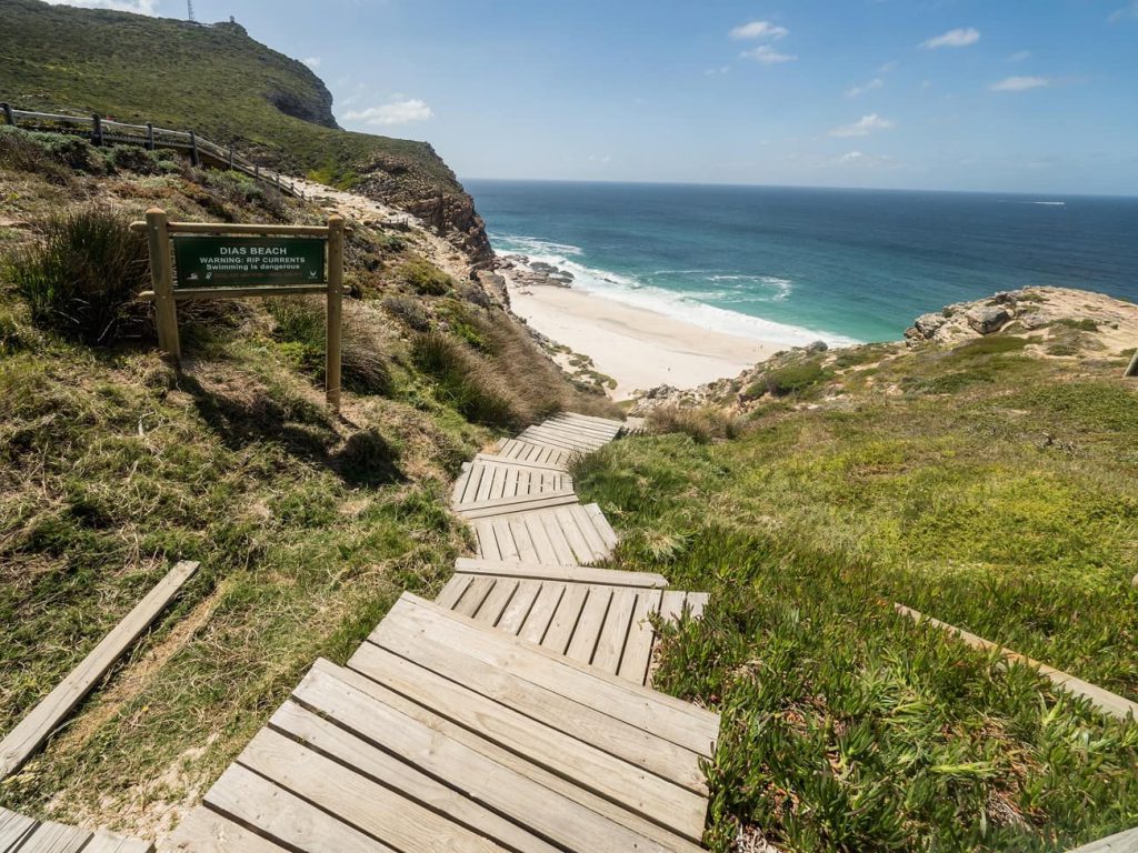 מדרגות עץ יורדות לחוף ים ושלט 'dias beach'
