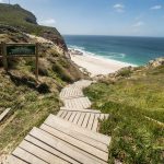 מדרגות עץ יורדות לחוף ים ושלט 'dias beach'