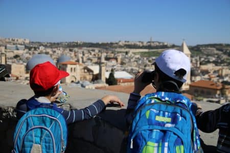 שני ילדים עם כובעים ותיקי טיול מביטים על נוף ירושלים ממעלה מגדל דוד