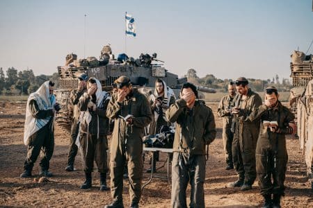 חיילים מתפללים תפילת שחרית בשטח, ברקע טנק עם דגל ישראל