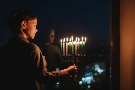 ילד מחזיק חנוכיה דולקת מול חלון