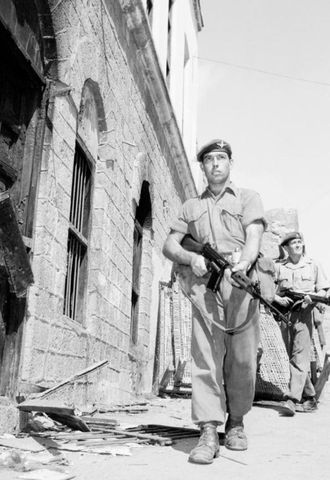 חיילים בריטים מפטרלים ליד שרידיו השרופים של בית כנסת ברובע קרייטר, בנובמבר 1956.